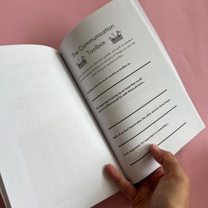 May include: An open book with a white background and black text. The book is titled "The Communication Toolbox". The text on the page includes the following: "The best time for us to resolve a conflict is...", "The best way to bring up an issue that could cause conflict would be with these phrases...", "Both of us feel heard when the other person does/says...", and "In an argument, it's important to remember...".