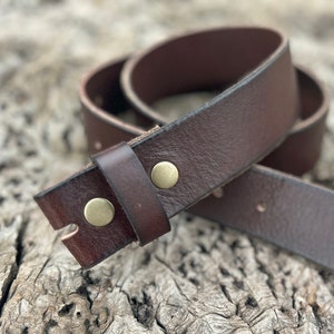 Puede incluir: Un cinturón de cuero marrón con dos hebillas de latón. El cinturón está enrollado y los extremos se superponen.