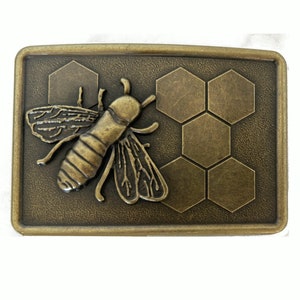 May include: A gold-toned metal belt buckle featuring a raised design of a bee on a honeycomb pattern.