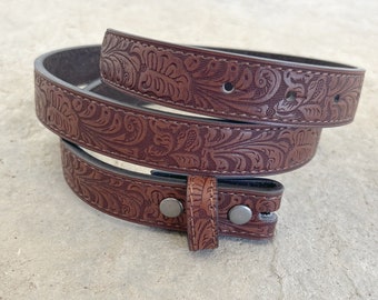 May include: A brown leather belt with a floral embossed design. The belt has a silver buckle and is rolled up.