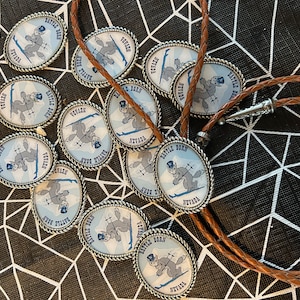 Puede incluir: Primer plano de un bolo de cuero marr&oacute;n con un dije de plata que representa una ardilla de dibujos animados esquiando con el texto "Battle Born Nevada". El dije est&aacute; rodeado de varios otros dijes similares.