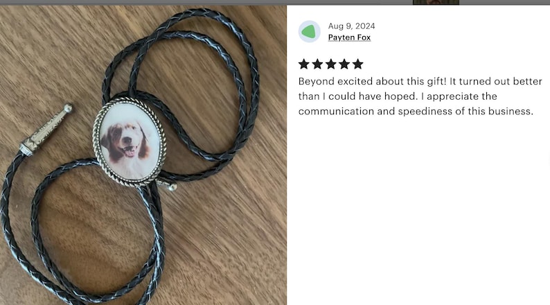 Puede incluir: Un corbat&iacute;n de cuero negro con un colgante ovalado de plata que presenta una foto de un perro marr&oacute;n y blanco. El colgante tiene un borde de plata.