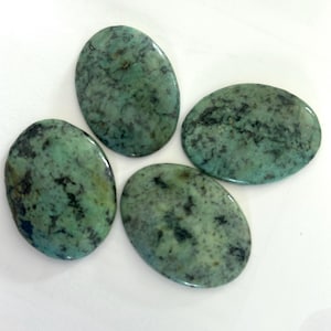 May include: Four polished, oval-shaped turquoise gemstones with a mottled pattern of green and black. The stones vary slightly in size and shape, each displaying a unique natural texture.