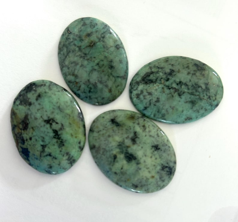May include: Four polished, oval-shaped turquoise gemstones with a mottled pattern of green and black. The stones vary slightly in size and shape, each displaying a unique natural texture.