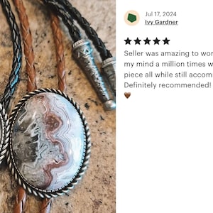 Puede incluir: Dos corbatas bolo con diferentes colgantes. Un colgante presenta una imagen en blanco y negro de una cabeza de caballo. El otro colgante presenta una piedra de &aacute;gata marr&oacute;n, blanca y gris. Ambos colgantes est&aacute;n engastados en metal plateado.