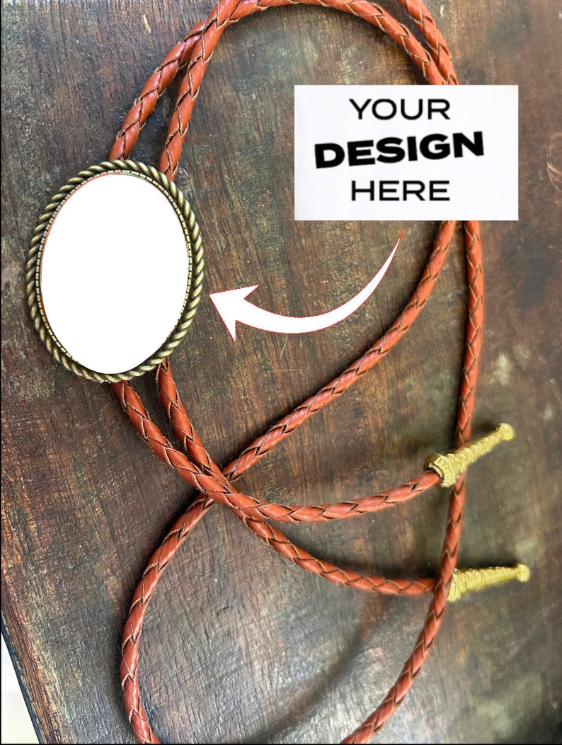 Puede incluir: Un corbat&iacute;n de cuero marr&oacute;n con un inserto redondo de cer&aacute;mica blanca. El inserto est&aacute; en blanco y tiene un marco de metal dorado. El texto "YOUR DESIGN HERE" est&aacute; sobre un fondo blanco.