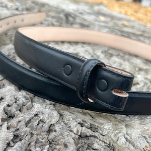 Puede incluir: Un cinturón de cuero negro con una hebilla simple y un acabado liso.