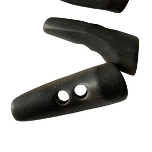 May include: Three black plastic buttons with two holes each. The buttons are shaped like a long oval with rounded ends.