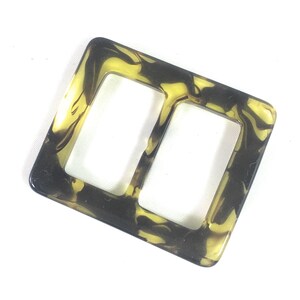 Puede incluir: Una hebilla de pl&aacute;stico marmoleado marr&oacute;n y amarillo con dos aberturas rectangulares.