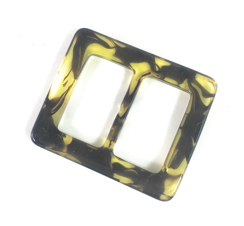 Puede incluir: Una hebilla de pl&aacute;stico marmoleado marr&oacute;n y amarillo con dos aberturas rectangulares.