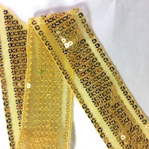 Könnte beinhalten: Gelber Paillettenbesatz mit einem Netzrücken. Der Besatz hat ein sich wiederholendes Muster aus goldenen Pailletten.