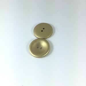 May include: Two gold-colored buttons with two holes each. The buttons are round and have a slightly raised center.