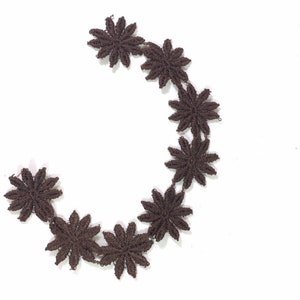 May include: A brown lace trim with a repeating flower design. The trim is made of delicate fabric and has a soft, feminine feel.