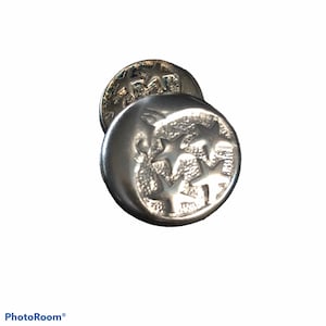 Puede incluir: Botón plateado con tres estrellas en un diseño circular.