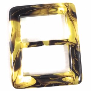 Puede incluir: Una hebilla de pl&aacute;stico marmoleado marr&oacute;n y dorado con un dise&ntilde;o de doble bucle.