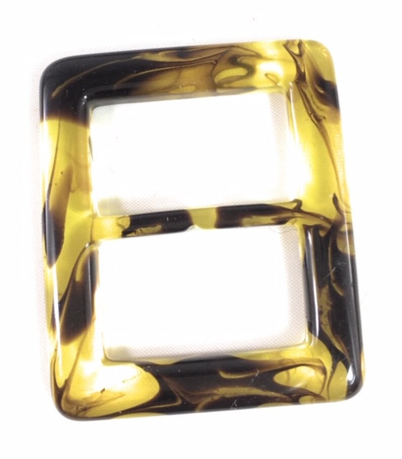 Puede incluir: Una hebilla de pl&aacute;stico marmoleado marr&oacute;n y dorado con un dise&ntilde;o de doble bucle.