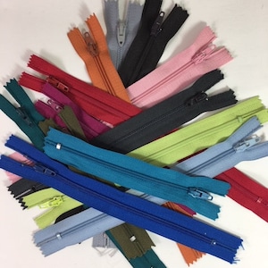 May include: Assortment of colorful zippers in various shades of blue, green, red, orange, pink, and black. The zippers are arranged in a pile on a white surface.