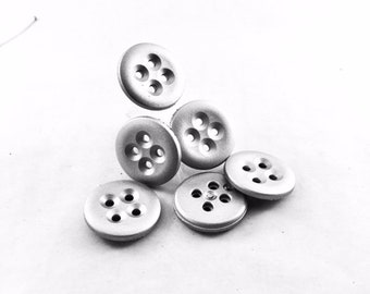 May include: Six silver buttons with five holes each. The buttons are arranged in a loose pile on a white surface.