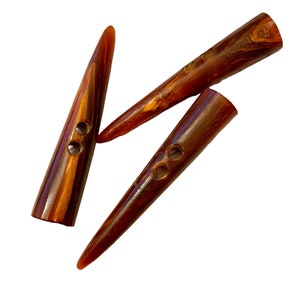 May include: Three brown horn buttons with two holes each. The buttons are pointed at one end and rounded at the other.