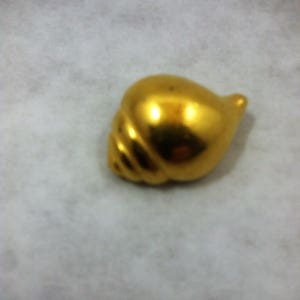 Puede incluir: Una concha de mar de color dorado con un acabado liso y brillante. La concha tiene un diseño en espiral y una punta puntiaguda.