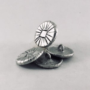 May include: Four silver metal buttons with a raised, circular, and textured design. The buttons have a square shape in the center.