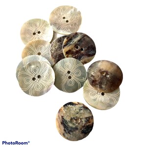 May include: A collection of 10 round, white and brown shell buttons with a decorative design. The buttons have two holes each.