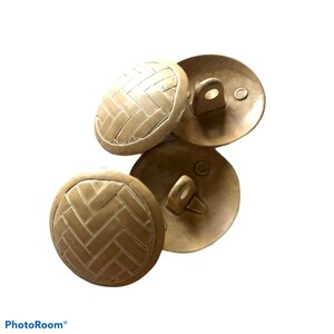 Puede incluir: Tres botones beige con un patrón tejido y un bucle en la parte posterior. Los botones están hechos de un material texturizado y tienen un diseño ligeramente elevado.