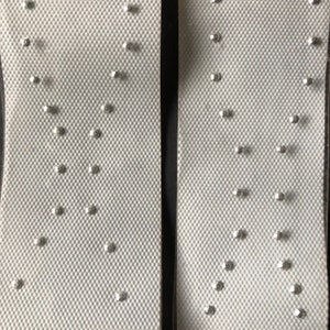 Könnte beinhalten: Zwei weiße Schuheinlagen mit Reihen kleiner silberner Nieten. Die Einlagen sind so konzipiert, dass sie Druck entlasten und die Füße stützen.