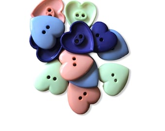 May include: A selection of heart-shaped buttons in pastel shades of pink, blue, and green. Each button features two or four holes for sewing. The buttons are arranged on a white background.