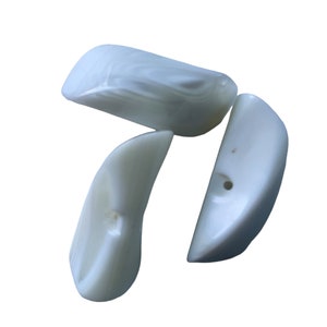 May include: Three white, smooth, pearlescent, shell-shaped beads with a hole in the center of each bead.