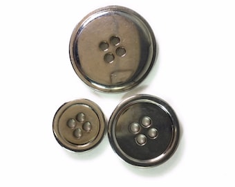 Puede incluir: Tres botones de metal plateado con cuatro agujeros cada uno. Los botones son de diferentes tamaños.