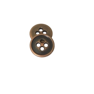 Peut inclure: Deux boutons en bronze antique avec quatre trous chacun. Les boutons ont un bord légèrement surélevé et un centre sombre, créant une esthétique vintage. Ces boutons sont idéaux pour les projets de couture, ajoutant une touche classique aux vêtements.