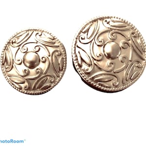 以下が含まれることがあります： 円形のデザインで、複雑なケルトの結び目と盛り上がった中心部が特徴の銀製のイヤリングのペアです。