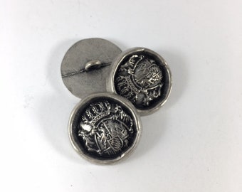 May include: Two silver-toned buttons with a raised design of a crown and coat of arms. The buttons are round and have a smooth surface.