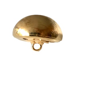 Puede incluir: Un botón dorado en forma de media esfera con una superficie texturizada y un ojal para coser. El botón es de metal y tiene un acabado brillante. El botón es un suministro de costura.