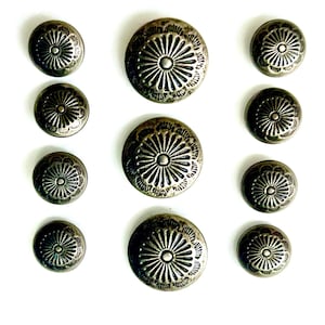 May include: Ten silver-toned metal buttons with a decorative floral design. The buttons are round and have a raised centre with a circular pattern.