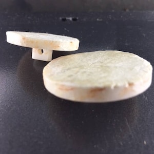 Puede incluir: Dos posavasos redondos de cerámica de color blanco roto con una textura ligeramente rugosa.