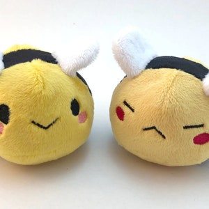 May include: Two plush bee toys with different facial expressions. One bee has a happy face with pink cheeks and a smile. The other bee has a grumpy face with red cheeks and a frown.