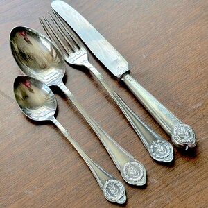 May include: A set of four silver-plated cutlery pieces, including a knife, fork, and two spoons. The cutlery has decorative handles with a leaf design.