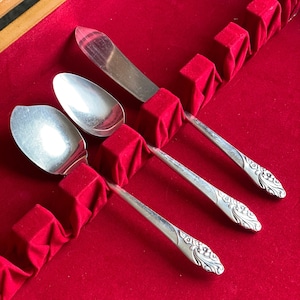 Può includere: Tre cucchiai d'argento con manici decorati sono esposti in una scatola foderata in velluto rosso. I cucchiai sono disposti in fila con i manici rivolti verso lo spettatore.