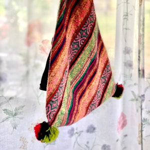 May include: A colourful triangular bag with a geometric pattern in shades of red, pink, green, blue, and yellow. The bag has a tassel on each corner.