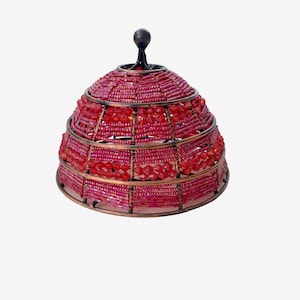 May include: A dome-shaped food cover featuring a dark bronze metal frame with horizontal bands of small, faceted, translucent red beads. The structure is topped with a small, dark bronze spherical finial, creating a decorative, semi-circular mesh design.