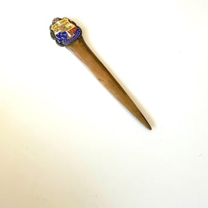 May include: A vintage letter opener with a brass blade and a decorative handle. The handle features a colorful enamel crest with the word "DANMARK" in blue. The opener is designed for opening envelopes and is a collectible item.
