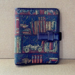 May include: A blue and brown patterned fabric wallet with a black leather strap. The pattern features books, a car, and other decorative elements.