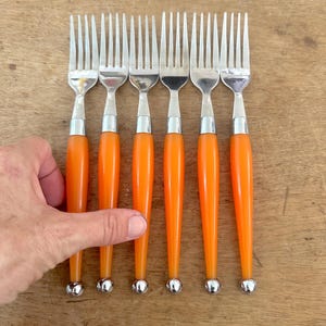 May include: A set of six stainless steel forks featuring bright orange cylindrical handles. Each fork has a polished metal finish on the tines and a small, spherical silver-toned metal bead at the base of the handle, creating a uniform appearance.