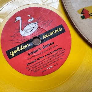 May include: A yellow vinyl record with a red label featuring a white swan and the text "golden records swan's dance (From Tschaikowsky's Swan Lake Ballet) Mitchell Miller and Orchestra For non-commercial use on phonographs in home only. Made in U.S.A. Copyright 1950 by Western Printing and Lithographing Company. Distributed by Simon and Schuster, Inc. trade R50B mark"