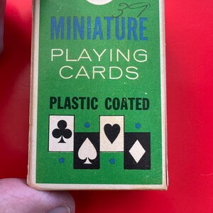 May include: A miniature deck of playing cards in a green box with blue and white text. The box features the words "MINIATURE PLAYING CARDS PLASTIC COATED" and card suit symbols. The number "39" is written in the top right corner.