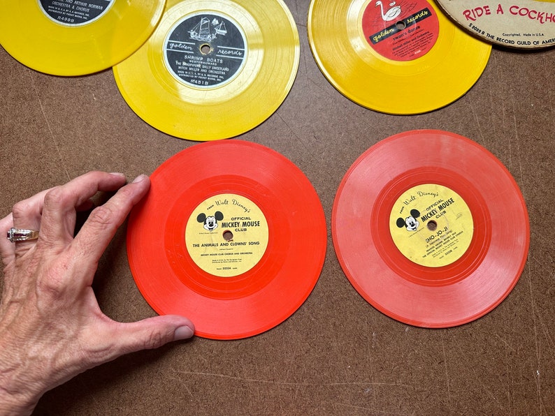May include: Two red vinyl records with yellow labels featuring Mickey Mouse and the text "Walt Disney's Official Mickey Mouse Club". One record has the text "The Animals and Clown's Song" and the other has the text "CHO-10-24".