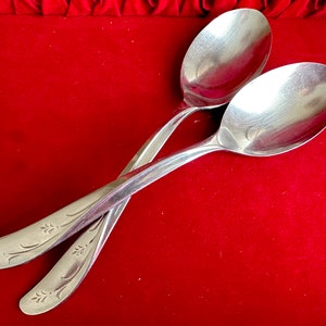 May include: Two silver spoons with ornate floral designs on a red velvet background.