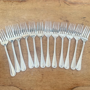 Könnte beinhalten: Eine Ansammlung von Silber-Gabeln auf einer Holzoberfläche. Die Gabeln haben ein klassisches Design mit langen, schlanken Zinken und tropfenförmigen Griffen. Die Anordnung deutet auf ein Ess- oder Servier-Set hin.